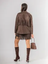 Chaqueta de estilo boho confeccionada en ecocuero agamuzado, con diseño de flecos en el frente, cierre frontal con botones y bolsillos laterales. Presenta un corte holgado y forro interior.
