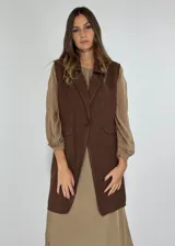 Chaleco largo color beige, con cuello solapa, un botón frontal y dos bolsillos de parche. Presenta costuras decorativas en contraste.