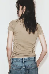 Camiseta corta de cuello redondo y manga corta, color gris oscuro, con frunces laterales ajustables mediante cordones.