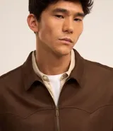 Campera masculina de estilo casual con cuello inglés, cierre frontal por cremallera, bolsillos laterales y ajuste elástico en el bajo. Presenta detalles de recortes en la parte superior delantera.