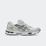 Championes Asics modelo Gel Nyc, en color blanco con detalles en gris claro y azul marino. Confeccionados con malla transpirable y superposiciones sintéticas, con tecnología GEL en la suela para mayor comodidad.
