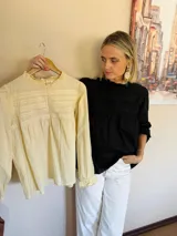 Blusa negra de manga larga con detalles de encaje y frunces en el pecho. Presenta cuello redondo con volados y puños con elástico y volado.