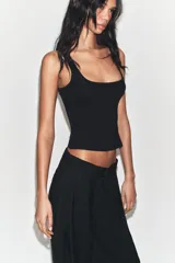 Pantalón negro de tiro alto y pernera ancha, confeccionado en tejido fluido, con bolsillos laterales y detalles de pliegues en la parte delantera.