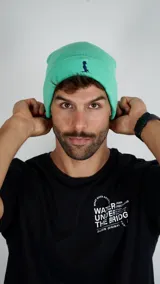 Gorro tipo beanie de tejido de punto en color verde agua, con diseño de doblez y logo bordado en azul marino en la parte frontal.