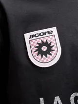 Remera negra de manga corta y cuello redondo, de corte holgado. Cuenta con estampado frontal de estilo deportivo que incluye la inscripción "LA GRACIOSA", un parche circular con diseño de sol y el logo de la marca.