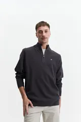 Buzo de tejido de punto color verde oliva, con cuello alto y cierre frontal parcial. Presenta un pequeño logo bordado en el pecho.