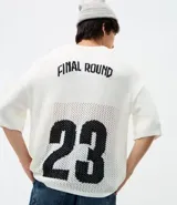Remera de corte oversized confeccionada en tejido jacquard de color blanco con textura calada. Presenta mangas cortas, cuello redondo y un diseño gráfico deportivo con el número 23 en color negro en la parte frontal.