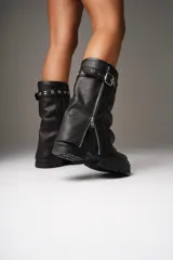 Botas de cuero negras con caña media, base de plataforma y cierre lateral con cremallera. Presentan una correa con hebilla y ojales metálicos en la parte superior de la caña. La caña mide 30 cm y la base 6 cm.