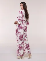 Enterito largo de calce fluido con escote en V cruzado, mangas 3/4 anchas, cintura elastizada con lazo ajustable y pantalón wide leg con bolsillos laterales. Estampado tipo toile de Jouy en tonos violeta sobre fondo blanco.