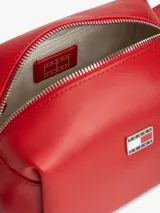 Bandolera Tommy Jeans de color rojo, diseño estructurado de silueta cuadrada con acabado liso. Cuenta con cierre de cremallera, correa ajustable y un colgante lateral de cordón trenzado con adorno en forma de corazón. Incluye la insignia con el logo de la marca en la parte delantera.