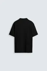 Polo negro de manga corta con cuello solapa y abertura frontal. Presenta un tejido jacquard con textura geométrica sutil.