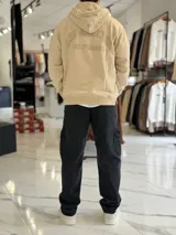 Canguro oversize beige con capucha y cordones ajustables, bolsillo tipo canguro y pequeño bordado en el pecho.