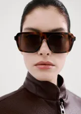 Chaqueta estilo bomber de cuero sintético marrón oscuro, con cierre frontal de cremallera, cuello alto abotonado y bolsillos frontales con solapa.