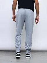 Pantalón de jogging gris melange con puños ajustados en los tobillos y cordón en la cintura. Presenta el logo Umbro bordado en negro en la pierna izquierda.