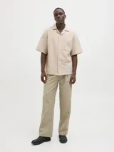 Camisa de manga corta color beige con cuello resort y cierre de botones. Confeccionada en tejido jacquard con mezcla de algodón y lino.