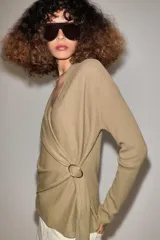 Chaqueta de punto de color tostado, con escote en V y manga larga. Diseño cruzado al frente con cinturón lazada en el mismo tejido y detalle de hebilla metálica circular en el lateral.