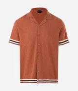 Camisa de punto jacquard color naranja, con cuello solapa, manga corta y cierre frontal con botones. Presenta detalles de rayas horizontales en contraste en el ruedo y en los puños de las mangas.