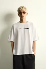 Camiseta de corte holgado con cuello redondo y manga corta. Presenta un diseño frontal con la frase New York Essence combinando tipografía cursiva y letras en bloque con efecto relieve.
