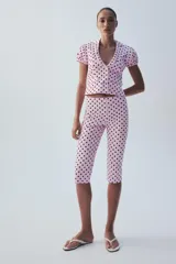Chaqueta corta rosa con estampado de lunares negros, de cuello solapa y manga corta abullonada. Cuenta con falsos bolsillos con solapa en el delantero y cierre frontal con botones.
