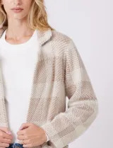 Chaqueta de tejido suave con estampado a cuadros en tonos beige y blanco, cuello con solapa y cierre de botón frontal. Incluye bolsillos delanteros.