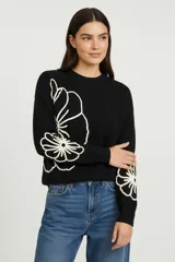 Sweater negro de tejido de punto con diseño holgado, cuello redondo a la base y mangas largas. Presenta apliques bordados en color crema con motivos florales que se extienden desde el costado hacia las mangas.