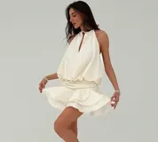 Vestido corto color marfil de corte holgado, con cuello halter y detalle de abertura frontal tipo gota. La parte superior es amplia y fluida, complementada con una falda corta de volados escalonados.