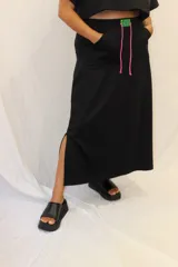 Falda larga de estilo deportivo confeccionada en tejido de algodón y poliéster. Presenta cintura elástica con cordón de ajuste en color fucsia, bolsillos laterales y un aplique decorativo de acrílico en la parte frontal.