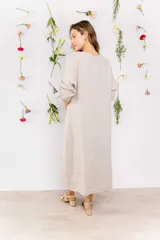 Vestido midi de lino color beige, con corte recto, cuello redondo y mangas 3/4 con botón. Presenta una hilera de botones decorativos en el frente y un tajo lateral.