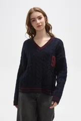 Sweater de tejido de punto con diseño de trenzas, cuello en V y detalles de rayas en contraste en cuello, puños y ruedo. Presenta un número bordado en el frente y tiene un corte holgado.