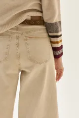 Pantalón de jean color beige claro, tiro alto, de corte ancho (wide leg) y largo hasta el tobillo con dobladillo. Presenta costuras verticales marcadas en el frente de las piernas.