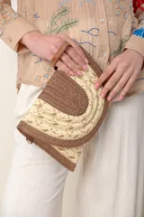 Sobre de mano o clutch de rafia con diseño semicircular. Presenta una combinación de colores: borde y secciones tejidas en marrón oscuro, y centro en rafia natural con detalles dorados (lurex) en tejido. Incluye un asa de mano de cuero marrón.