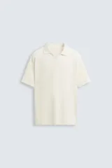 Polo de manga corta color crema, con cuello solapa y abertura frontal en forma de V. Presenta un tejido texturizado con patrón geométrico sutil.