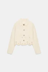 Cazadora color rosa pálido, de cuello solapa y manga larga. Tiene bordados perforados a tono en el ruedo y cierre frontal con botones color madera.