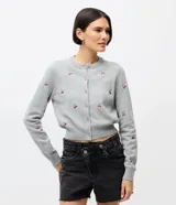 Cardigan corto de punto color gris, con cuello redondo, mangas largas y cierre frontal con botones. Presenta un diseño ajustado al cuerpo con bordados de cerezas distribuidos por toda la prenda.