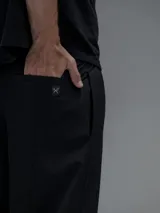 Pantalón cargo negro de corte oversize, confeccionado en microfibra elastizada. Presenta cintura elástica, bolsillos laterales y un bolsillo cargo con cierre de broche a presión. Incluye un sistema de elásticos con tancas en los tobillos para ajustar la apertura.