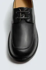 Zapato náutico de piel color negro con diseño liso, detalle de bordón en el empeine, horma cuadrada y suela con ligero tacón.
