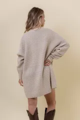 Buzo tipo sweater de punto color blanco, con diseño de trenzas verticales, cuello redondo, mangas largas y tajos laterales. Presenta un corte oversize y largo extendido.