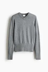 Buzo de punto fino color gris melange, con escote en V y remate acanalado ancho en puños y bajo.
