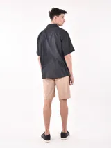 Camisa de manga corta color blanco roto con textura de tejido de lino o similar, corte holgado y cuello camisero.