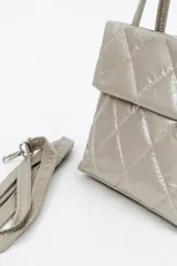 Cartera acolchada negra de material sintético con efecto brillante y costuras en rombos. Cuenta con solapa frontal y una correa corta de cadena gruesa de eslabones plásticos negros.