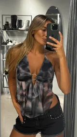 Top halter de tela liviana con estampado tie-dye en tonos grises, negros y rosados. Presenta un escote pronunciado con un aro metálico central y frunces que generan caída en la parte inferior.