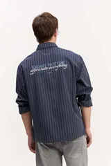 Camisa de manga larga azul marino con diseño de rayas verticales blancas, cuello clásico y estampa con bordado en la espalda.