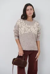 Buzo de tejido de punto en color beige, con cuello redondo y mangas largas. Presenta un delicado bordado de ramas y hojas en color crema en la parte superior del frente.