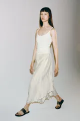 Falda midi fluida de tiro medio, color blanco, con cintura elástica ajustable mediante cordones y bajo asimétrico.