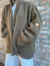 Campera de corderito color verde oscuro, con diseño holgado, cuello alto y manga larga. Presenta una etiqueta de cuero sintético en la manga.