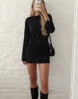 Vestido corto negro con espalda descubierta estilo cowl back, tirante horizontal posterior y mangas largas.