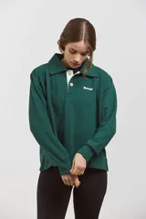 Buzo de algodón en color verde inglés, con diseño de cuello tipo chomba con botones frontales y detalles en blanco. Presenta un corte holgado y cómodo con mangas largas.