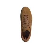 Championes adidas modelo Gazelle, confeccionados en gamuza color marrón con las icónicas tres tiras laterales en tono a juego. Presentan suela de goma color caramelo y el nombre del modelo grabado en dorado en el lateral.