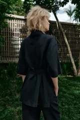 Chaqueta de estilo safari confeccionada en mezcla de lino, color azul marino, con cuello solapa, mangas cortas y cierre frontal con botones ocultos. Presenta bolsillos de parche en el pecho con solapa y botones, además de un cinturón ajustable del mismo tejido para anudar en la cintura.