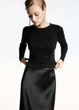 Jersey de punto fino color negro, con cuello redondo y manga larga. Presenta un diseño crop con aplicación de strass distribuido por toda la prenda.